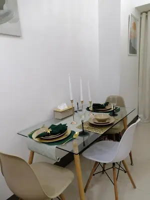 a dining room with a glass table and white chairs at Vistaro Stays at Fame Residences in Manila