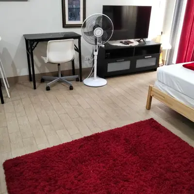 a bedroom with a red rug and a desk and a fan at Cozy Gutz Place at 16th in Manila