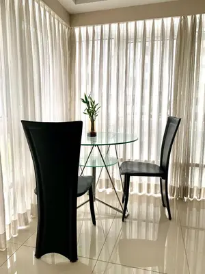 a glass table and two chairs in a room with curtains at MaxStays - Max Home at Fort Victoria Tower A in Manila