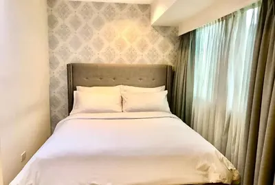 a bed with white sheets and pillows next to a window at MaxStays - Max Home at Fort Victoria Tower A in Manila