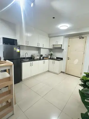 a kitchen with white cabinets and a black refrigerator at Les Chambres Cosy - Sea Residences MOA PASAY in Manila
