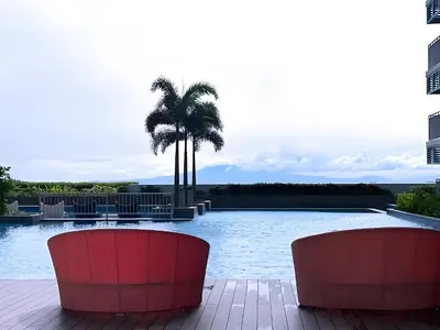 a swimming pool with two red chairs and a palm tree at Modern 1BR with Magnificant Garden View, Near Airports, Okada, Solaire with Free Parking in Manila