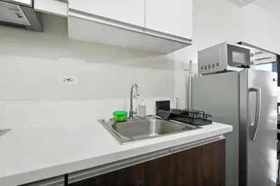 a white kitchen with a sink and a refrigerator at Makati Penthouse Studio with City Views in Manila