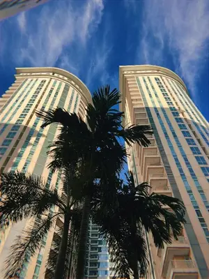 two tall buildings with a palm tree in the foreground at Upscale Stylish Suite Near BGC and View of Venice Grand Canal Mall in Manila