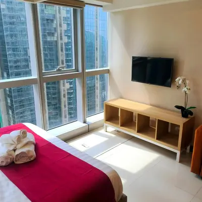 a bedroom with a bed and a tv and large windows at Cozy Modernistic 1 BR Uptown BGC in Manila