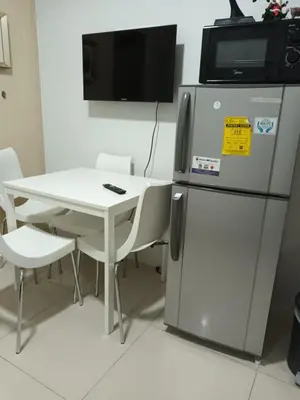 a kitchen with a table and a refrigerator with a tv on top at Sea Residences By Queen in Manila
