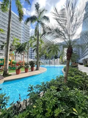 a swimming pool with palm trees and a fountain at Sparkling Shell Residences Kaeri Properties in Manila
