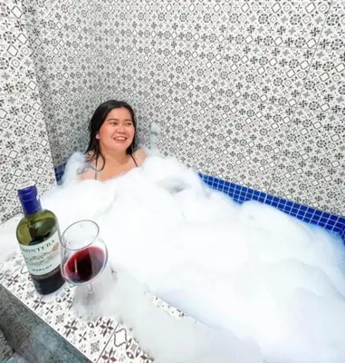 a woman sitting in a bath tub with a glass of wine at Valley Mansions Staycation near Taytay in Cainta