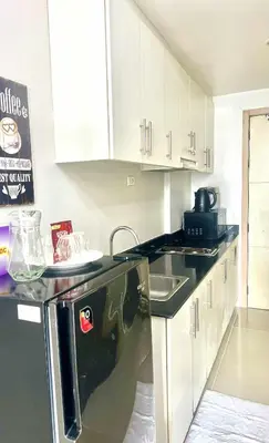a kitchen with white cabinets and a black dishwasher at Eden Era staycation in Manila
