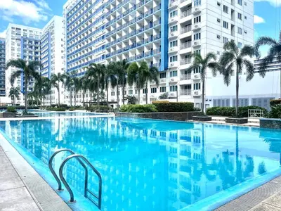a large swimming pool with palm trees and buildings at Premiere Haven MOA Staycation in Manila
