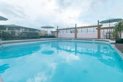 a large blue swimming pool with chairs and umbrellas at Urban Travellers Hotel by RedDoorz in Manila