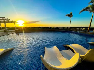 a pool with chairs and the sunset in the background at Luxury 1-Bedroom Apartment Across Okada Manila in Manila