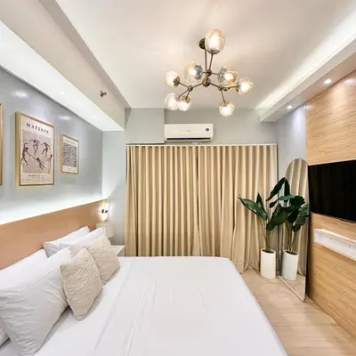 a bedroom with a white bed and a chandelier at Stylish Studio Unit with Balcony in Grace Residences in Manila