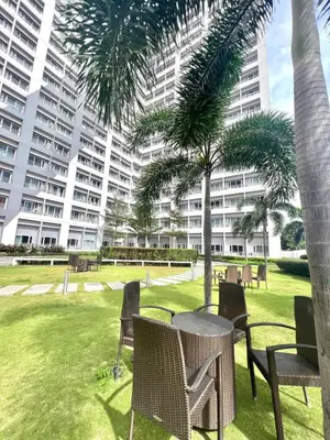 a park with chairs and palm trees and a large building at Stylish Studio Unit with Balcony in Grace Residences in Manila