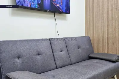 a couch in a room with a tv on a wall at City View Staycation Near Mall of Asia and Airport in Manila