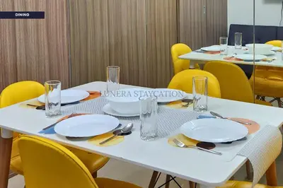 a table with yellow chairs and white plates and glasses at City View Staycation Near Mall of Asia and Airport in Manila