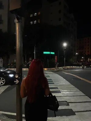 a woman with red hair standing on a street corner at night at Cozy Haven Across Terminal 3 in Manila