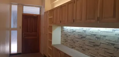 a kitchen with wooden cabinets and a stone wall at Nemar Ladies Dormitel in Manila