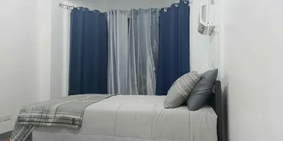 a bedroom with blue curtains and a bed with pillows at 1 bedroom condo unit for 4 with balcony, pool, WIFI at Newport across NAIA T3 in Manila