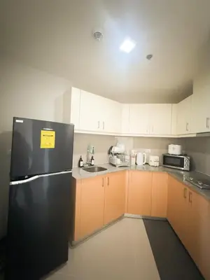 a kitchen with a black refrigerator and white cabinets at Uptown Parksuites Tower 2 in Manila