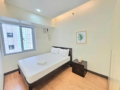 a bedroom with a bed with white sheets and a window at The Infinity Towers in BGC - Spacious 2 Bedroom - View, Washer, Fast WiFi in Manila