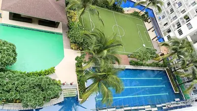an overhead view of a swimming pool with palm trees and a tennis court at Pool view from one-bedroom condo at Shore Residence in Manila