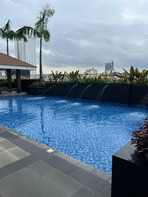 a large blue swimming pool with a fence and palm trees at Cozy 1 Bedroom unit in Manila in Manila
