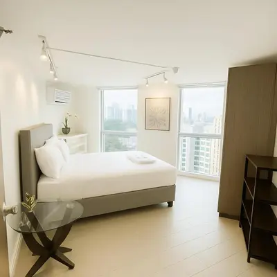 a white bedroom with a bed and a glass table at Cozy & Spacious 2BR Stay Near BGC - Home Theater in Manila