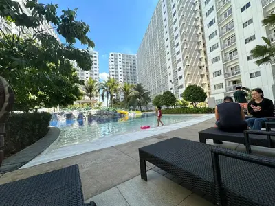 two people sitting on benches next to a swimming pool at Koro Den at Shore Residences in Manila