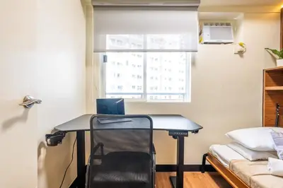 a desk in a room with a bed and a window at Prime 2-BR apartment near major business districts in Manila