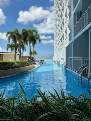 a swimming pool in front of a building with palm trees at Breeze Staycation by Charmed in Sampong