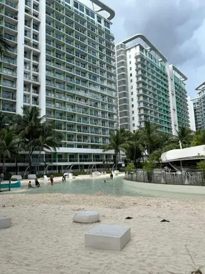 a beach with people in a swimming pool with tall buildings at Azure Urban Resort Residences - St Tropez Tower in Manila