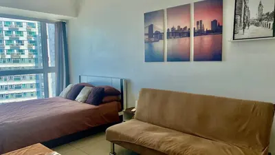 a bedroom with a bed and a couch and a window at High End Penthouse Makati CBD in Manila