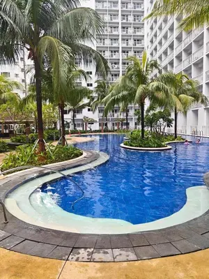 a large swimming pool with palm trees and a building at Shore Residences in Manila