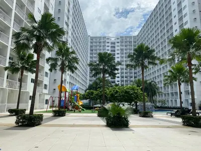 a park with palm trees and a playground in front of tall buildings at Shore - Spacious Room with Balcony - 52D in Manila