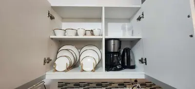 a kitchen with white cabinets with plates and coffee cups at Azure Luxe Suites in Azure Bicutan Near NAIA and MOA in Manila