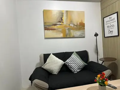 a living room with a black couch and a painting at Sweet Villa SMDC Breeze Residences Pasay in Manila