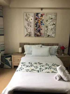 a bedroom with a large white bed with paintings on the wall at Condo Unit Near NAIA T3 in Manila