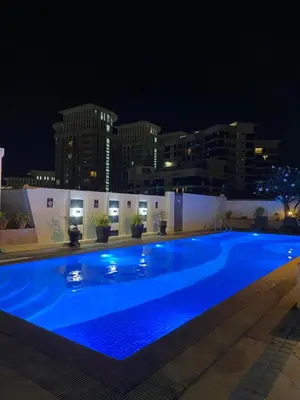 a large blue swimming pool at night with buildings at Cozy Cabin by JLS Near Venice Grand Canal Mall in Manila
