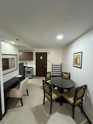 a living room with a table and chairs and a kitchen at A Venue Residences 80N in Manila