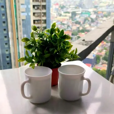 two coffee cups and a potted plant on a table at Cozy Modernistic 1 BR with Veranda! in Manila