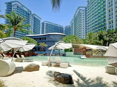 a beach with chairs and umbrellas in front of some buildings at Azure Urban Resort Residences Parañaque City near NAIA Airport in Manila