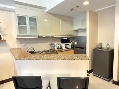 a kitchen with a counter with chairs and a refrigerator at Panoramic Views 2BR Family Stay in Mckinley BGC in Manila