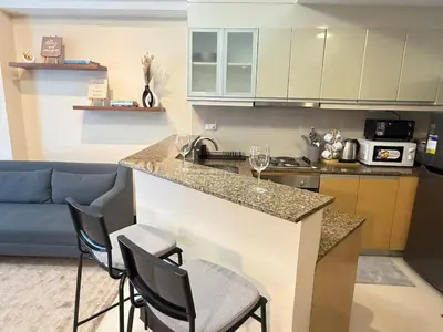 a kitchen with a sink and a counter with chairs at Panoramic Views 2BR Family Stay in Mckinley BGC in Manila