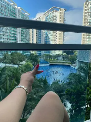 a woman sitting on a balcony looking out at a swimming pool at Positano Tower Beach view with PS4 - Azure Parañaque Resort in Manila