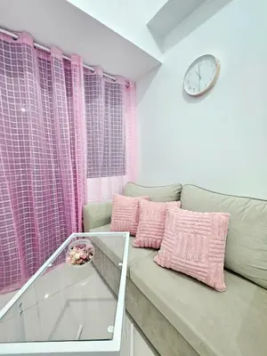 a living room with a couch with pink pillows and a clock at Cozy Modern Condotel in Pasay Near MOA & Airport in Manila