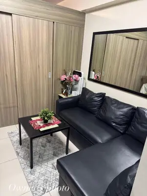 a living room with a black leather couch and a table at Juvrey Studio-Unit Breeze Residences in Manila