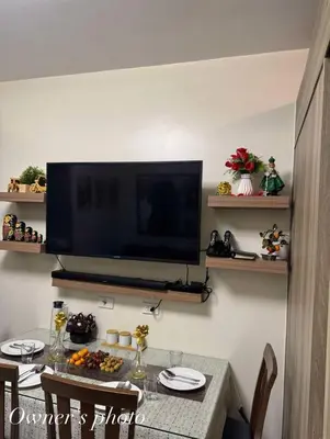 a living room with a table with a television on a wall at Juvrey Studio-Unit Breeze Residences in Manila