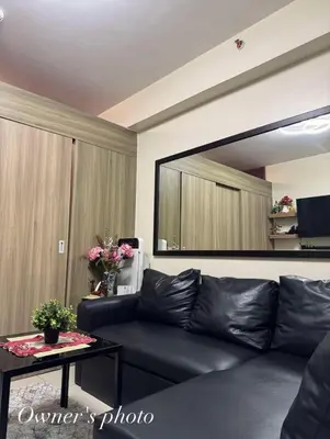 a black leather couch in a living room with a large mirror at Juvrey Studio-Unit Breeze Residences in Manila