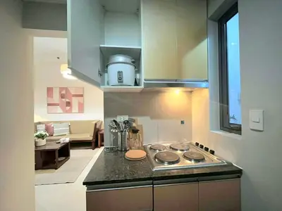 a kitchen with a stove top and a living room at Greenbelt Hamilton Residences by ChiKat in Manila